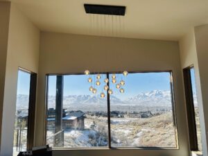 Cascading glass-orb chandelier installed over a great-room window framing snow-capped Utah mountains