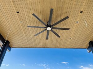 Large ceiling fan and recessed lighting on a wood-slat ceiling beneath a skylight