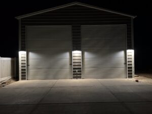 Wall-pack exterior lighting on a large detached metal shop at night